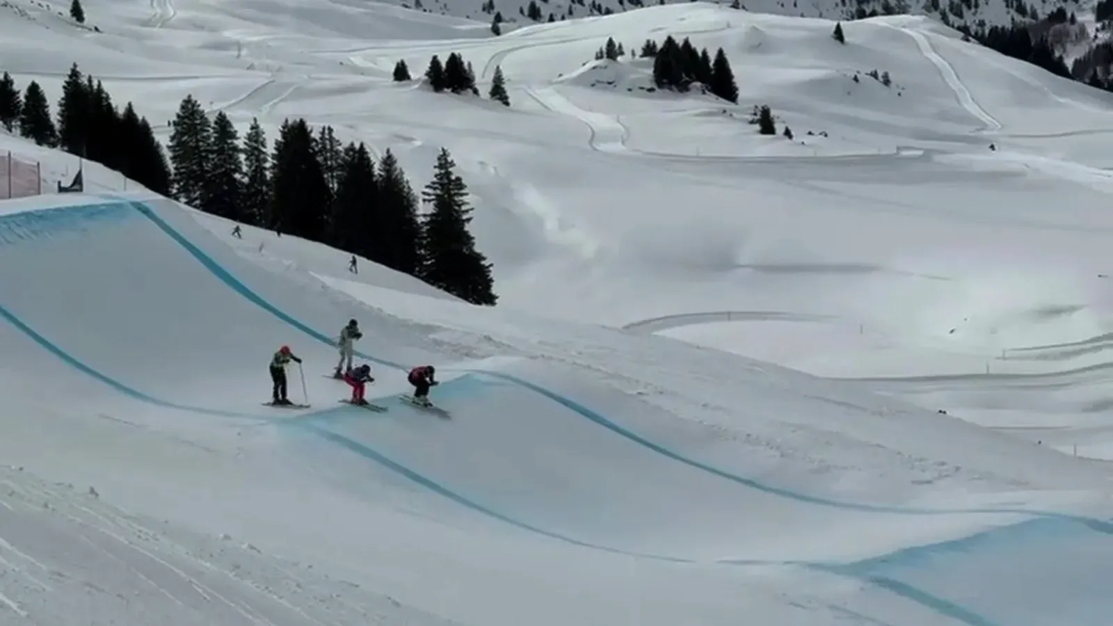 Vier Fahrer in einer Skicross-Rennsituation auf einer Strecke mit Steilkurve